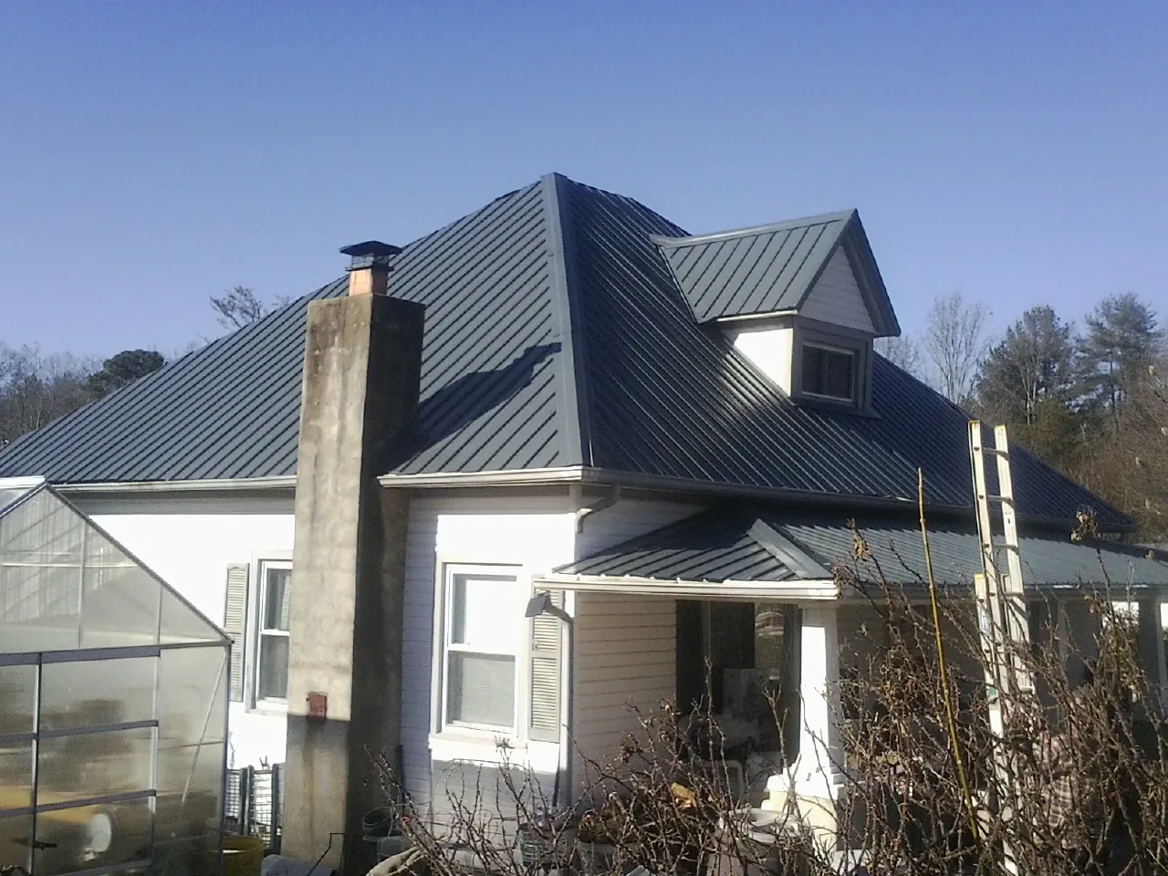 Dark blue standing seam metal roof on a white farmhouse with dormer — Slate & Tile Roof Repair by Roofing Brothers in Stateline