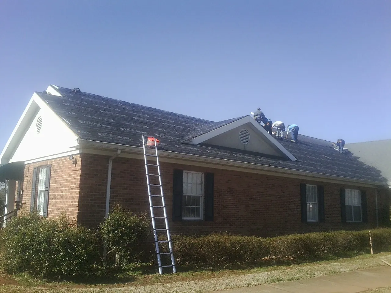 Crew tearing shingles off a brick ranch roof with a ladder set — Emergency Roof Repair work by our crew in Stateline