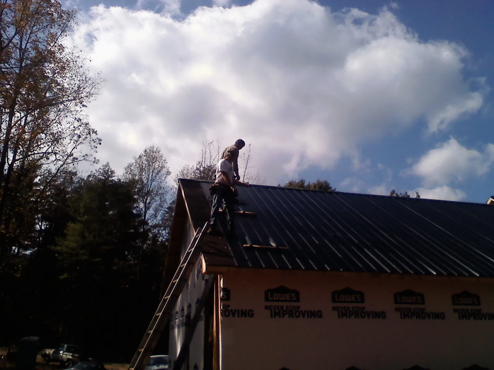 Roofer fastening dark metal panels high against a cloudy sky, from a Roof Inspection job in Stateline